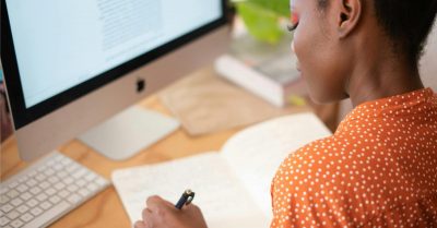 A woman at a computer station writing in her notepad