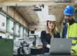 people in a warehouse or manufacturing building looking at a laptop